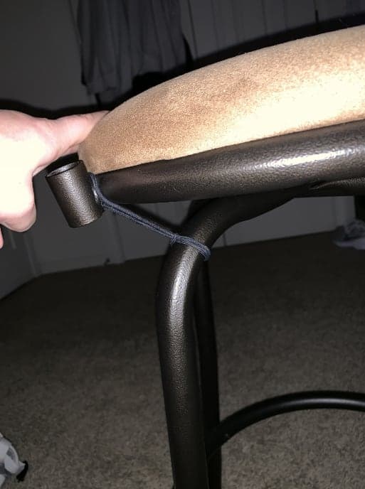 A padded stool seat being turned by hand on its base to test a swivel mechanism.