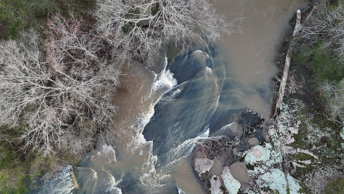 Top-down aerial view of whitewater rapids flowing between rocks and bare trees.